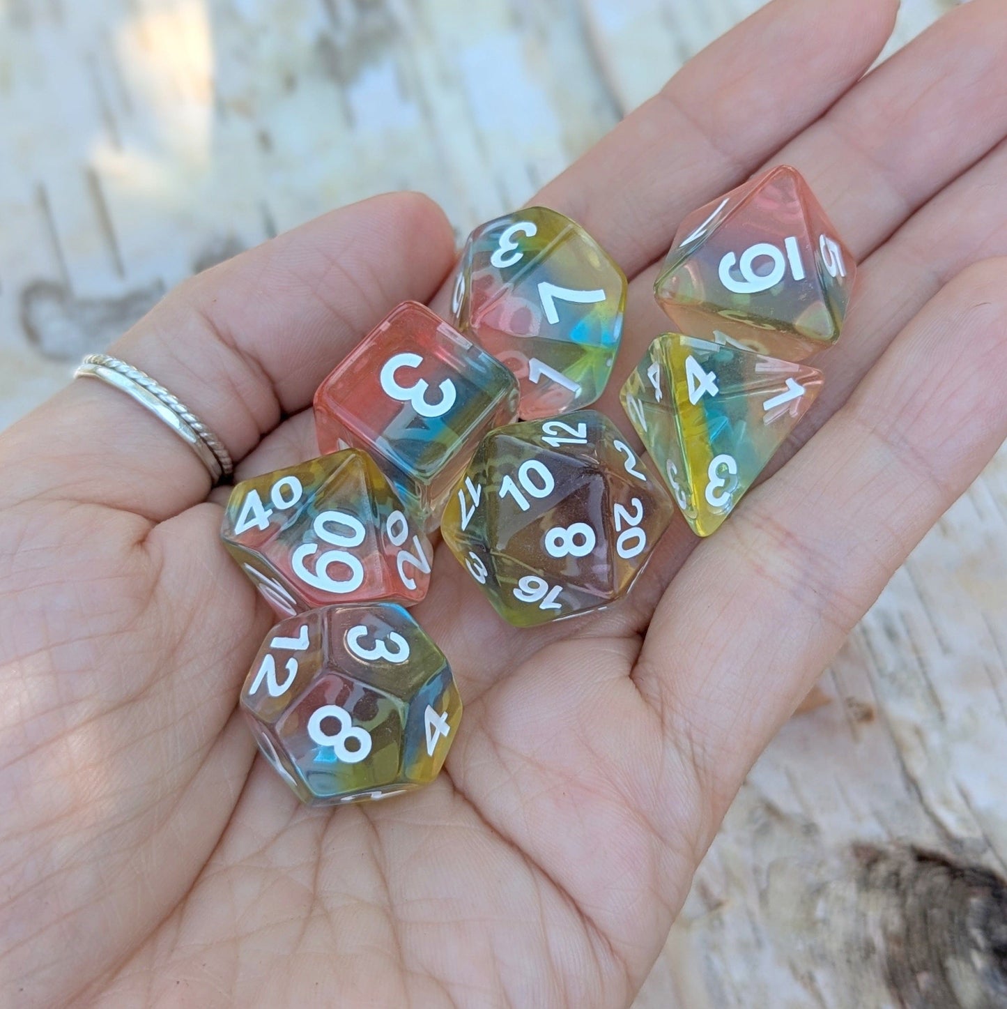 Hand holding Aurora Sky Dice Set with rainbow resin layers for tabletop games like Dungeons & Dragons.