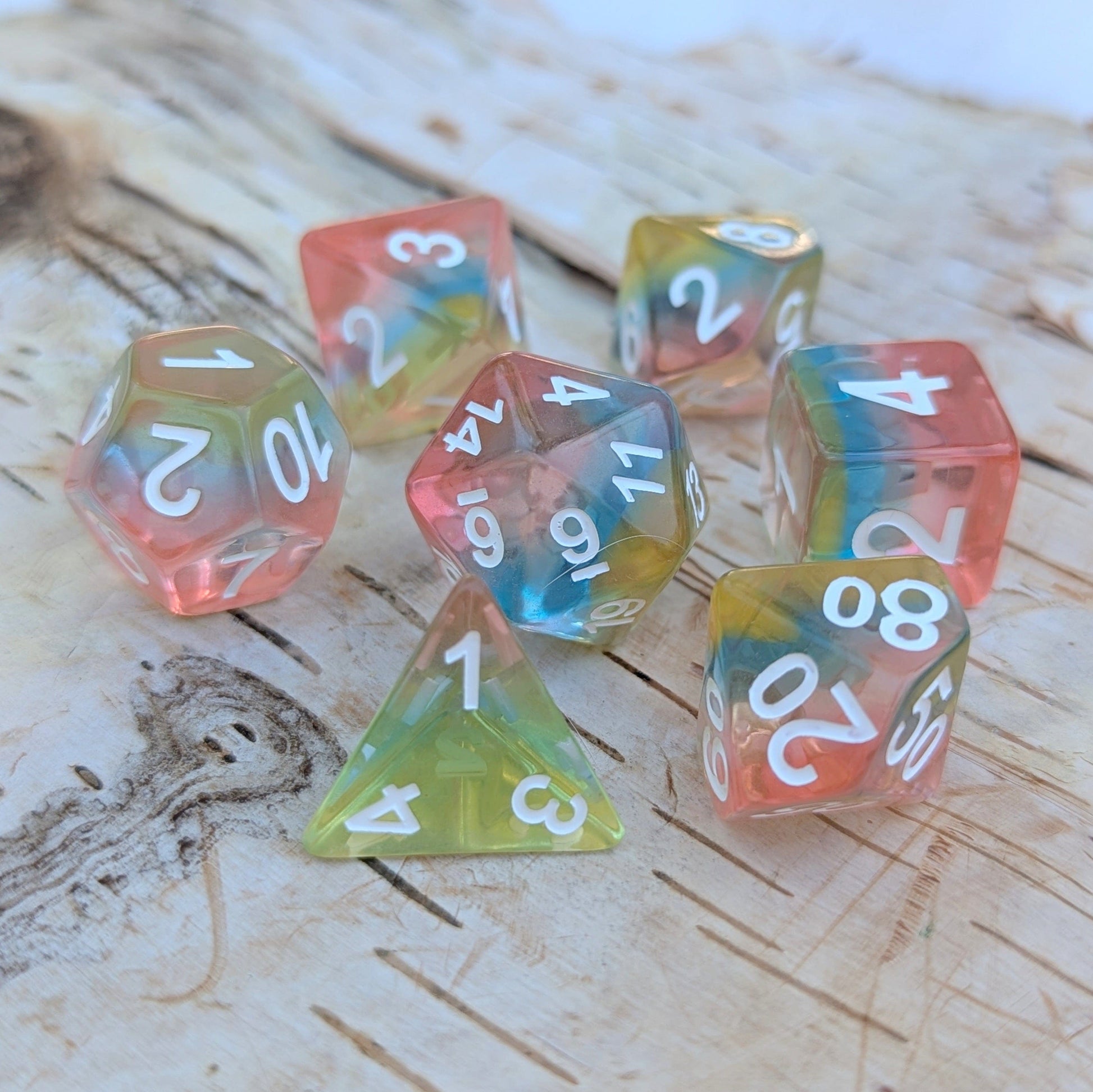 Aurora Sky Dice Set with rainbow resin layers, round edges, and white numbers on a wooden surface for tabletop role-playing games.