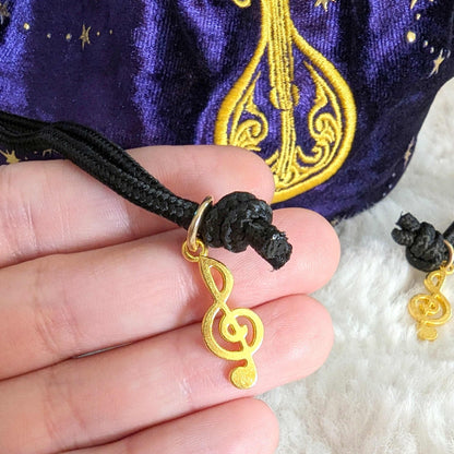 Close-up of enchanted lute embroidery on starry purple velvet bard dice bag with black cord drawstring and golden treble clef charm.