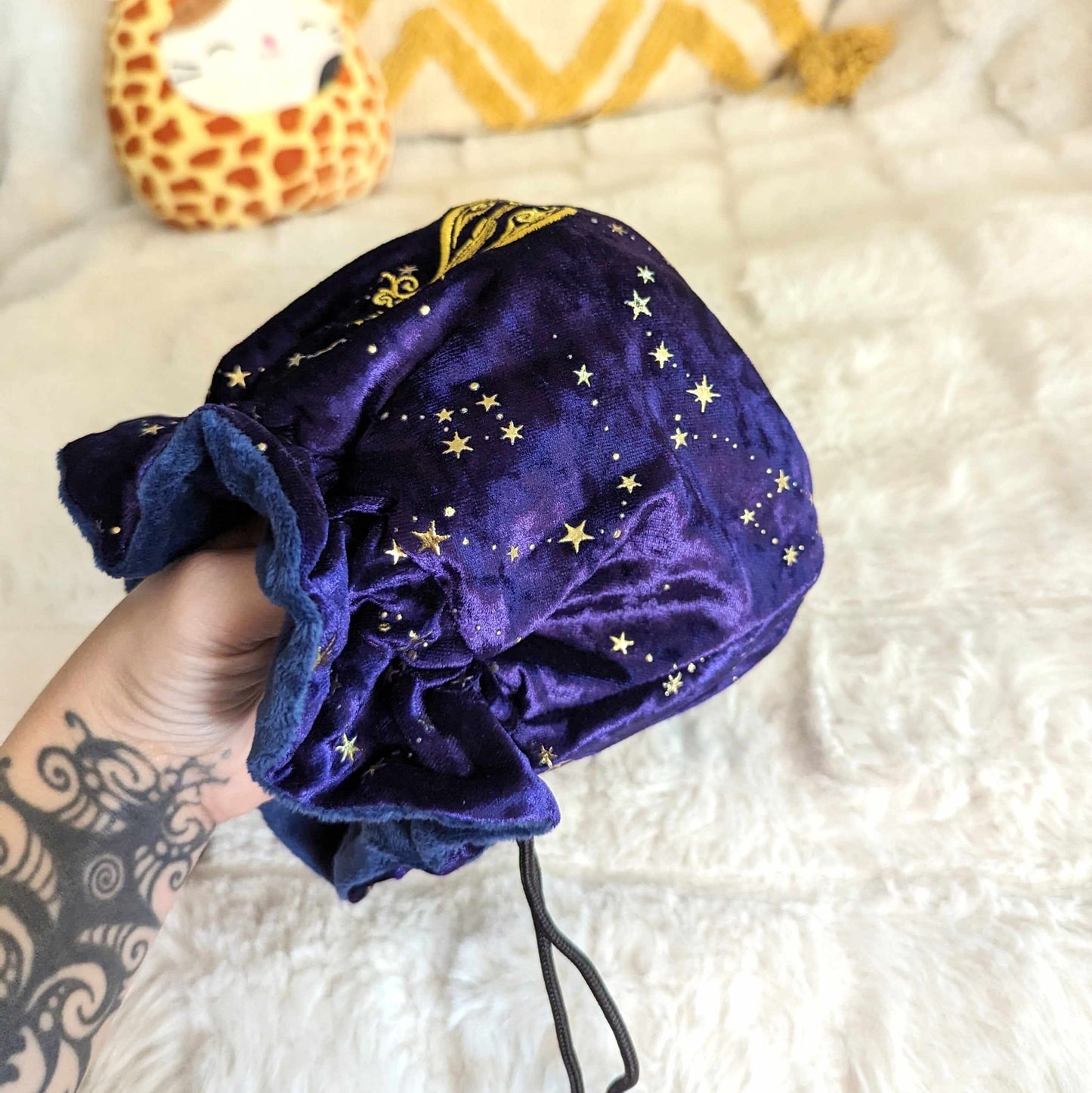 Purple starry velvet dice bag with embroidered enchanted lute design, featuring drawstrings and musical charms, held in hand.