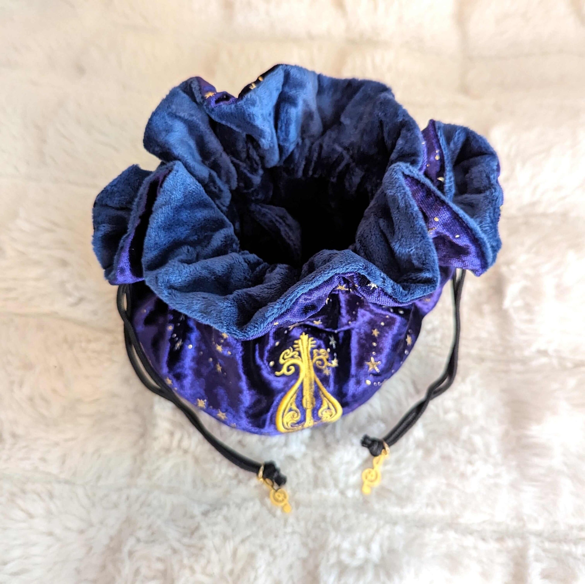 Purple bard dice bag with starry velvet, embroidered lute design, and musical charm drawstrings, ideal for storing dice sets.