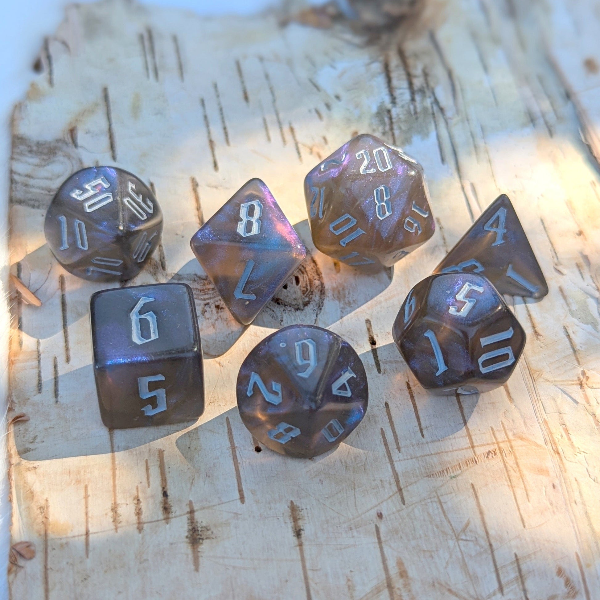 Black and blue glitter acrylic dice set with fantasy font for TTRPGs, featuring 7 polyhedral dice on a wooden surface.