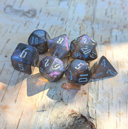 Black and blue glitter acrylic polyhedral dice set for TTRPGs, featuring fantasy font on a wooden surface.