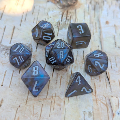 Black and blue glitter acrylic dice set with fantasy font on a wooden surface, 7-piece polyhedral set for tabletop RPGs like DnD.