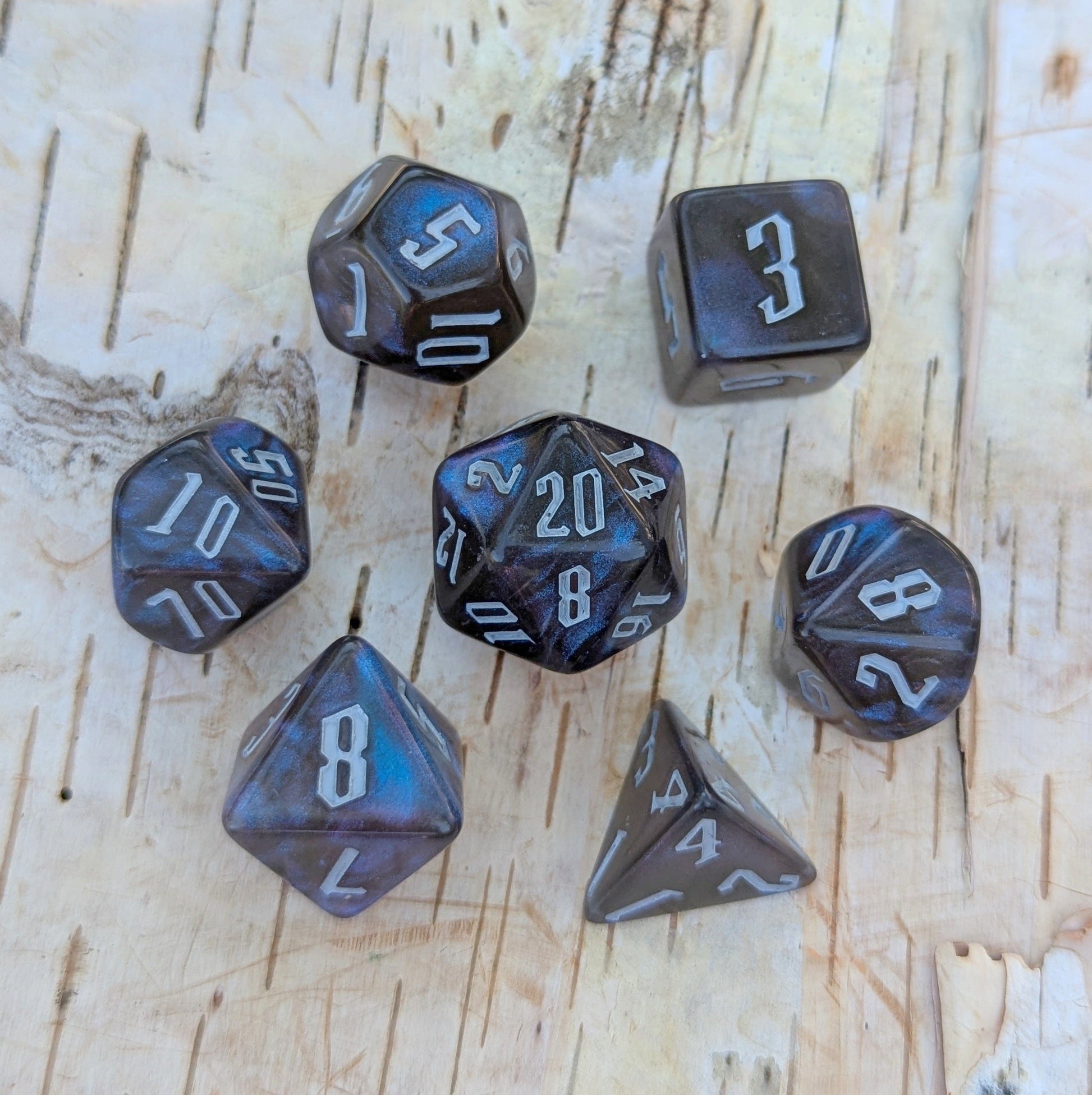 Black and blue glitter acrylic dice set with fantasy font, TTRPG 7 piece polyhedral dice for Dungeons and Dragons, on wooden surface.