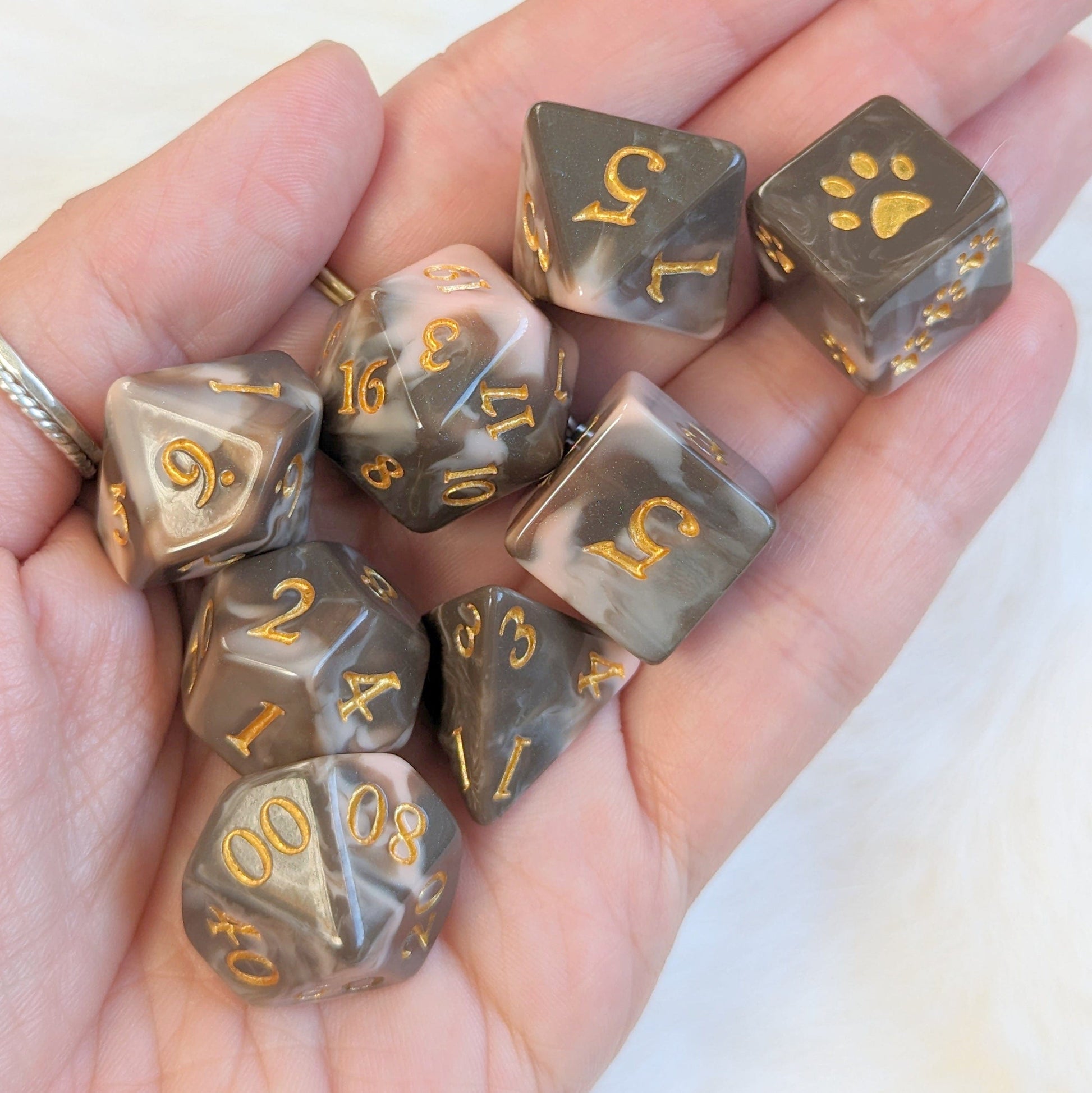 Hand holding Caramel Macchiato Dice Set, 8 Piece Chocolate Resin TTRPG Dice in rich caramel and cream hues with gold numbers.