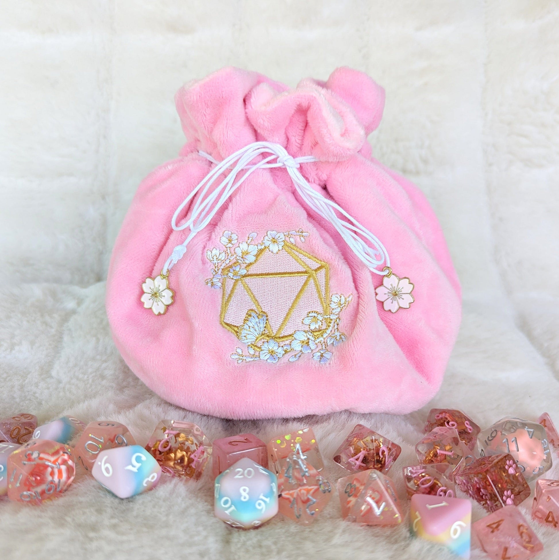 Pink cherry blossom dice bag with multi pockets, featuring embroidered D20 and butterfly design, surrounded by colorful dice.