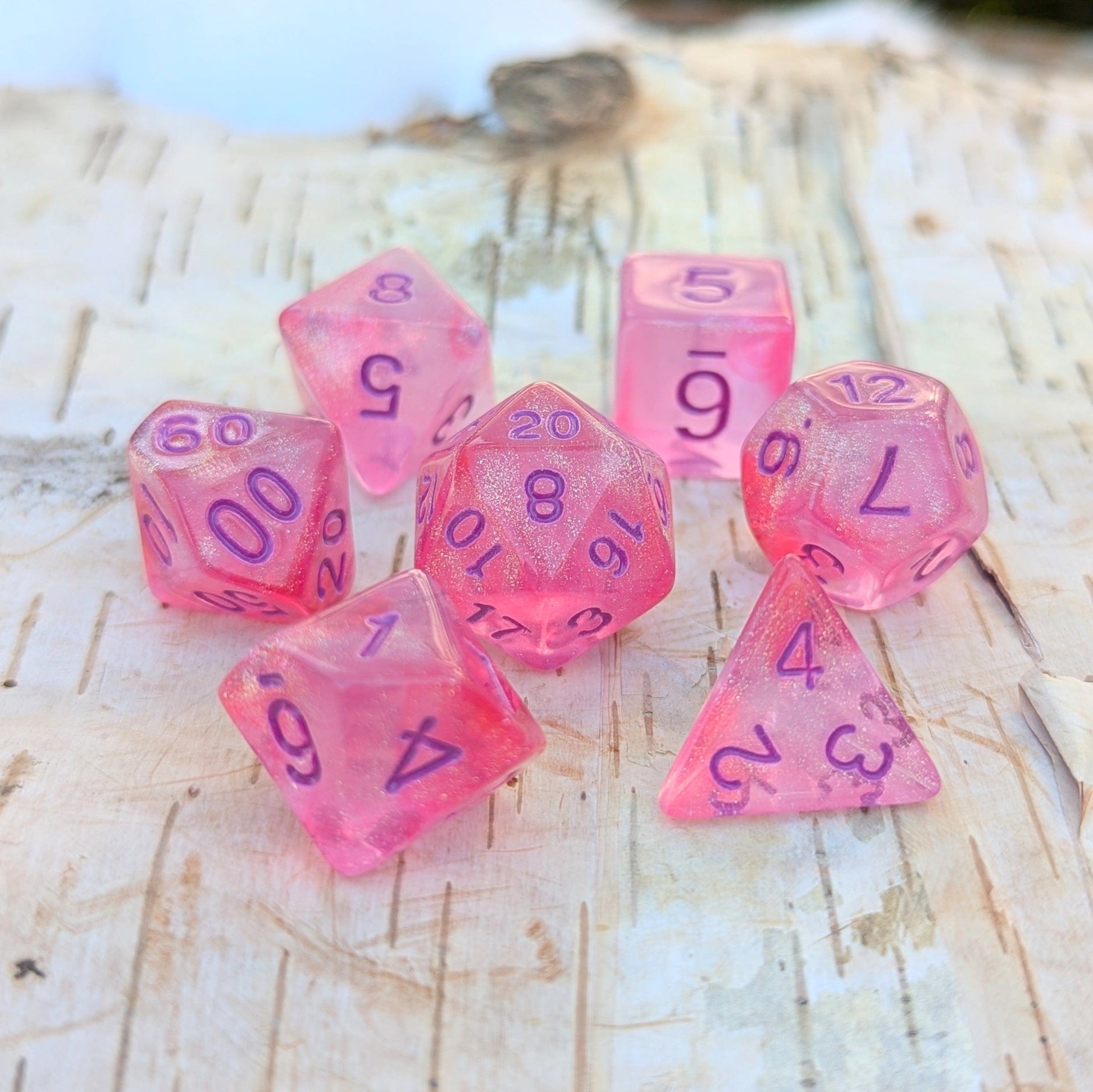 Bright pink Cheshire Will O Wisp 7 piece glitter dice set for TTRPGs like Dungeons and Dragons on a wooden surface.