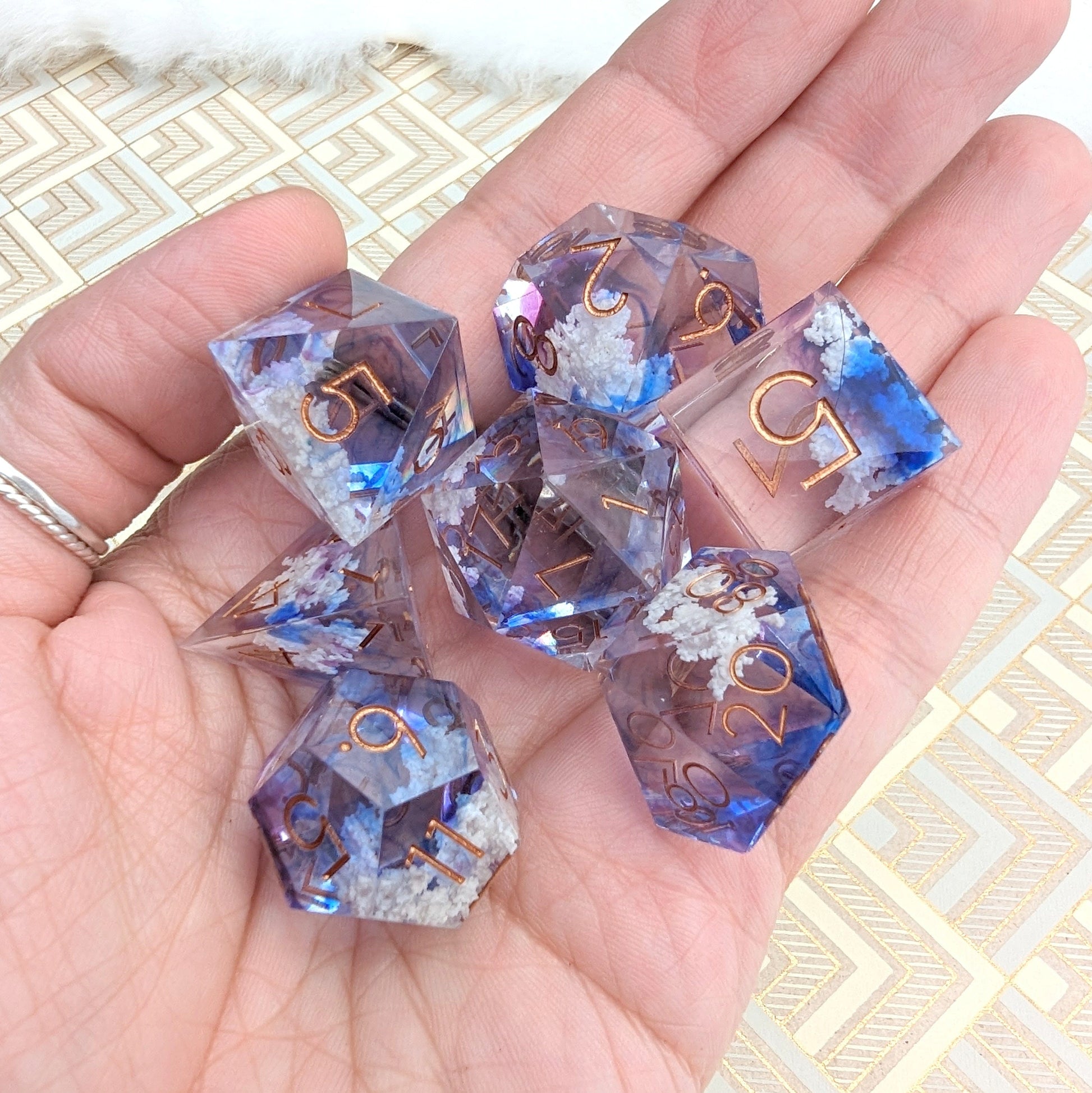 Hand holding Clouds Sharp Edge DnD Dice Set with blue and purple tints and cloud inclusions for tabletop role-playing games.