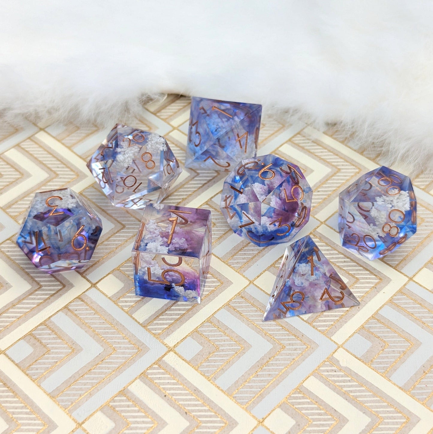 Clouds Sharp Edge DnD Dice Set with blue and purple tints and cloud inclusions on a patterned surface.