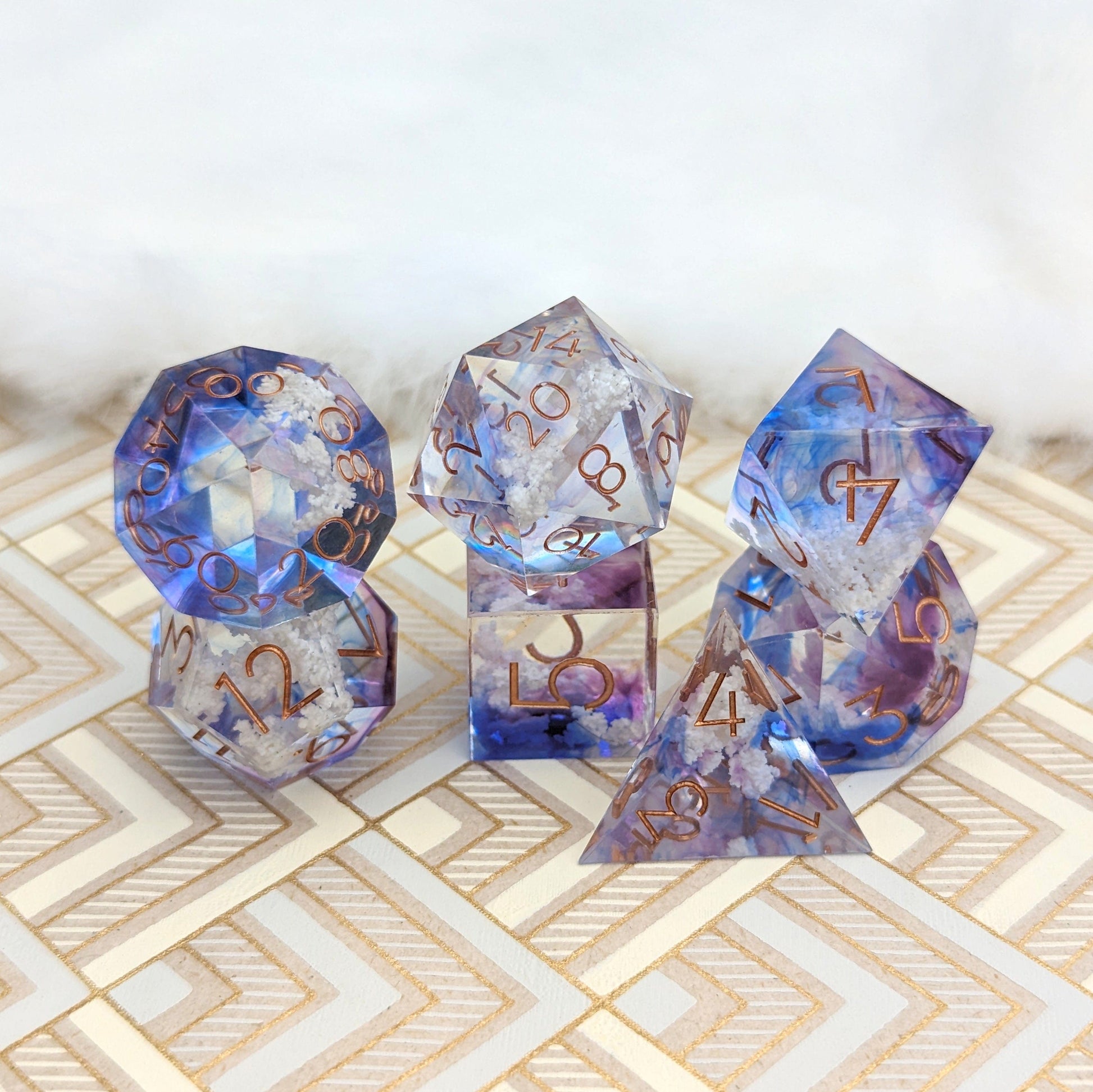 Clouds Sharp Edge DnD Dice Set with blue-purple tints and white cloud inclusions on a patterned surface.