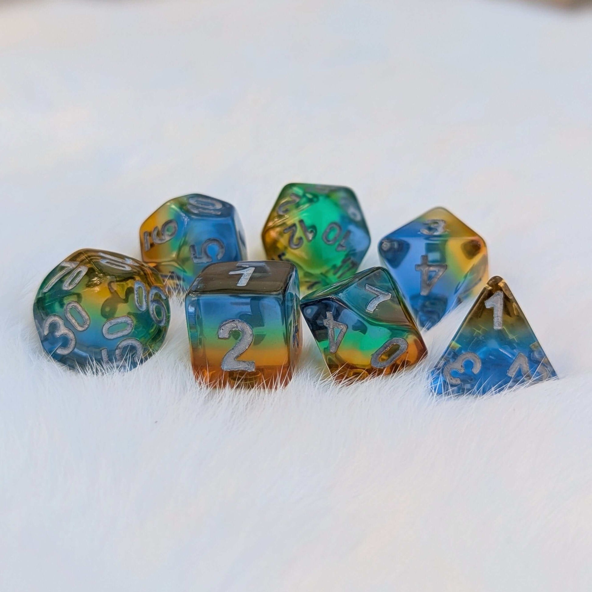 Vibrant rainbow layered TTRPG dice set with blue, green, yellow, and orange colors on a white furry background.