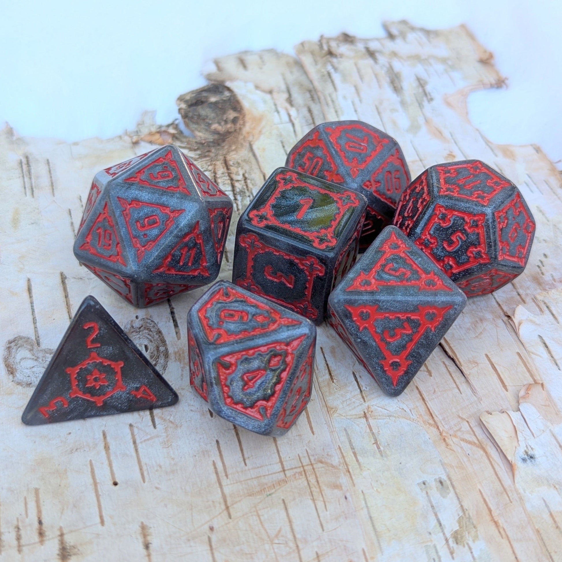 Dark Castle extra large glittering dark grey dice set with red numbers, 25mm 7-piece set on a rustic wooden background.