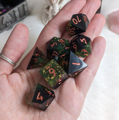 Dark green and black DnD dice set with gold flakes and copper font displayed in a hand for TTRPG games.