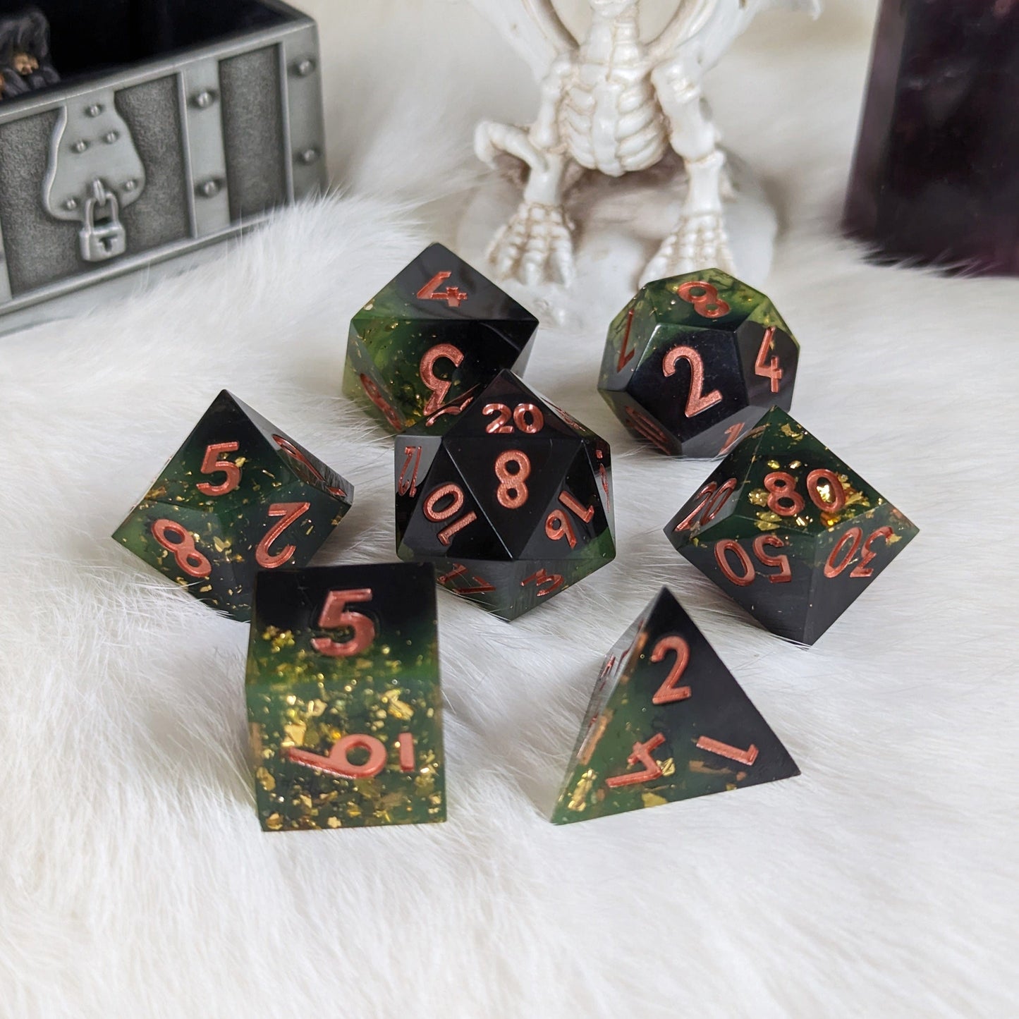 Dark green and black seven-piece DnD dice set with gold flakes and copper numbers on a white fur background.