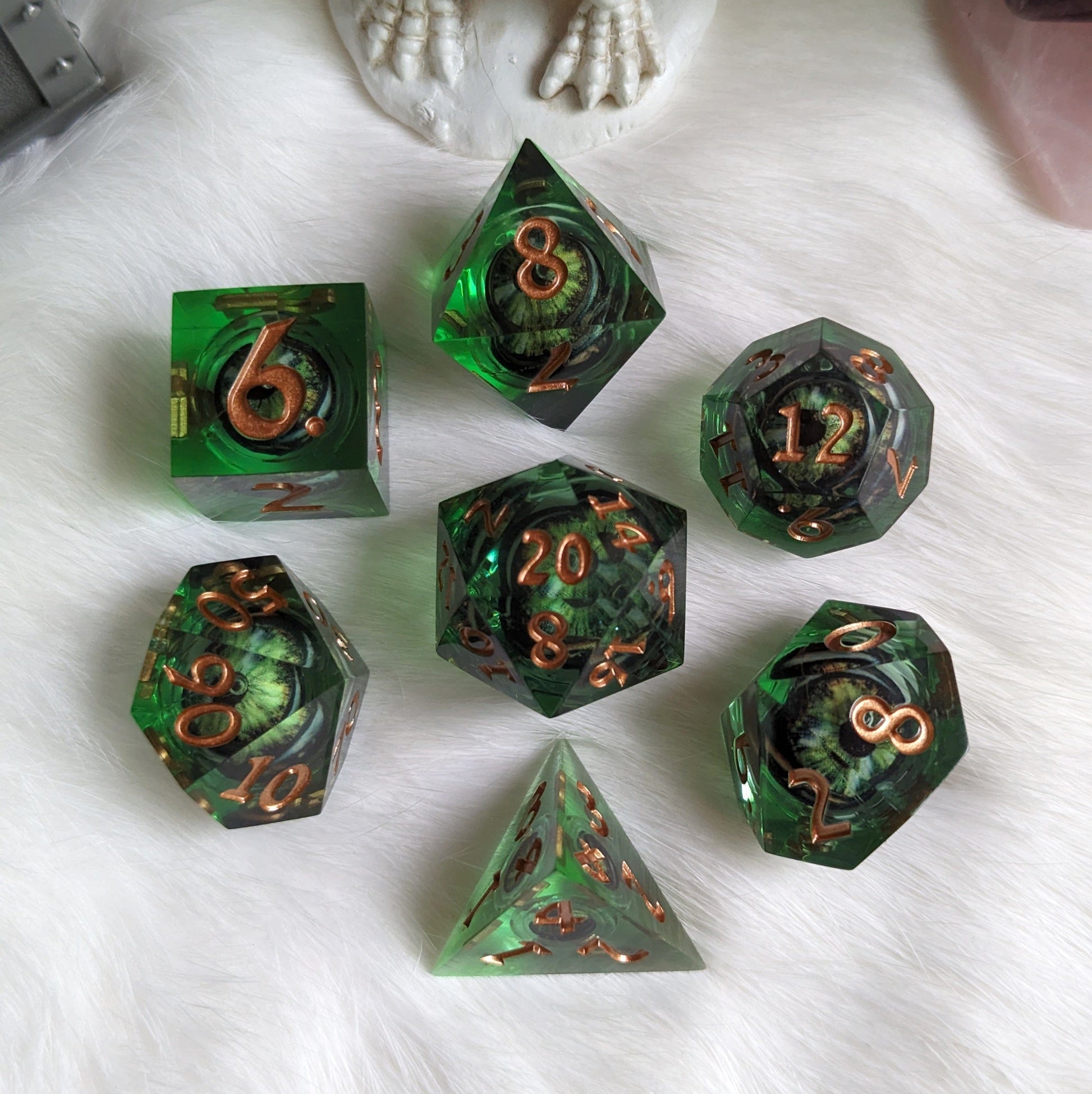 Dark green liquid core dice set with moving eyes for DnD, featuring sharp edges and copper numbers, on white surface.