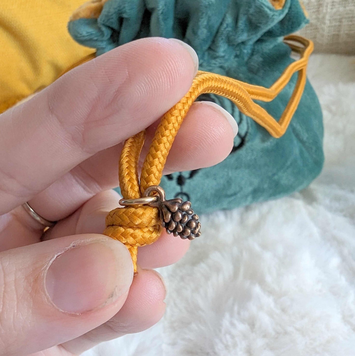 Close-up of a hand holding orange cord drawstring with pinecone bead on a plush green druid dice bag in the background.