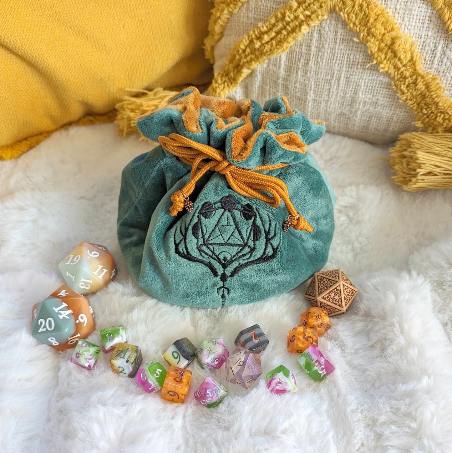 Green and brown druid dice bag with D20 moon phases embroidery and pinecone beads, surrounded by colorful dice on a cozy blanket.