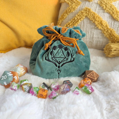 Green and brown druid dice bag with embroidered D20 and moon phases, surrounded by colorful dice on a soft surface.