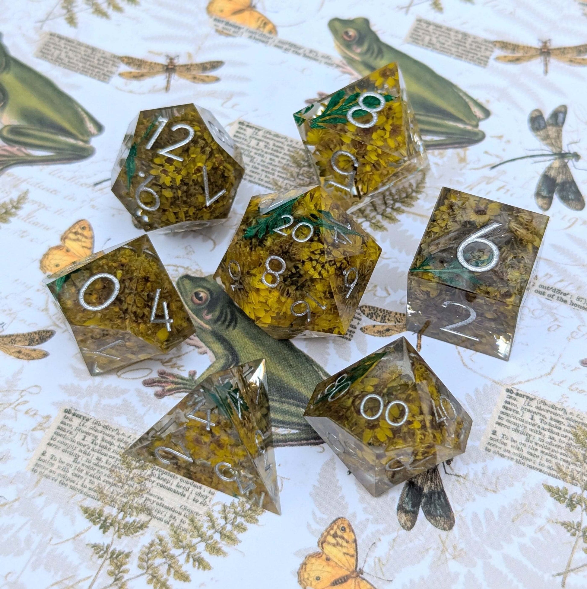 Enchanted Meadow DnD Dice Set with yellow flowers and green sprigs in resin, flawed sharp edge design, silver font on nature background.