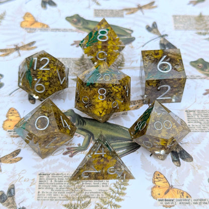 Enchanted Meadow flaw dice set with yellow flowers and green sprigs in clear resin, featuring sharp edges and silver numbers.