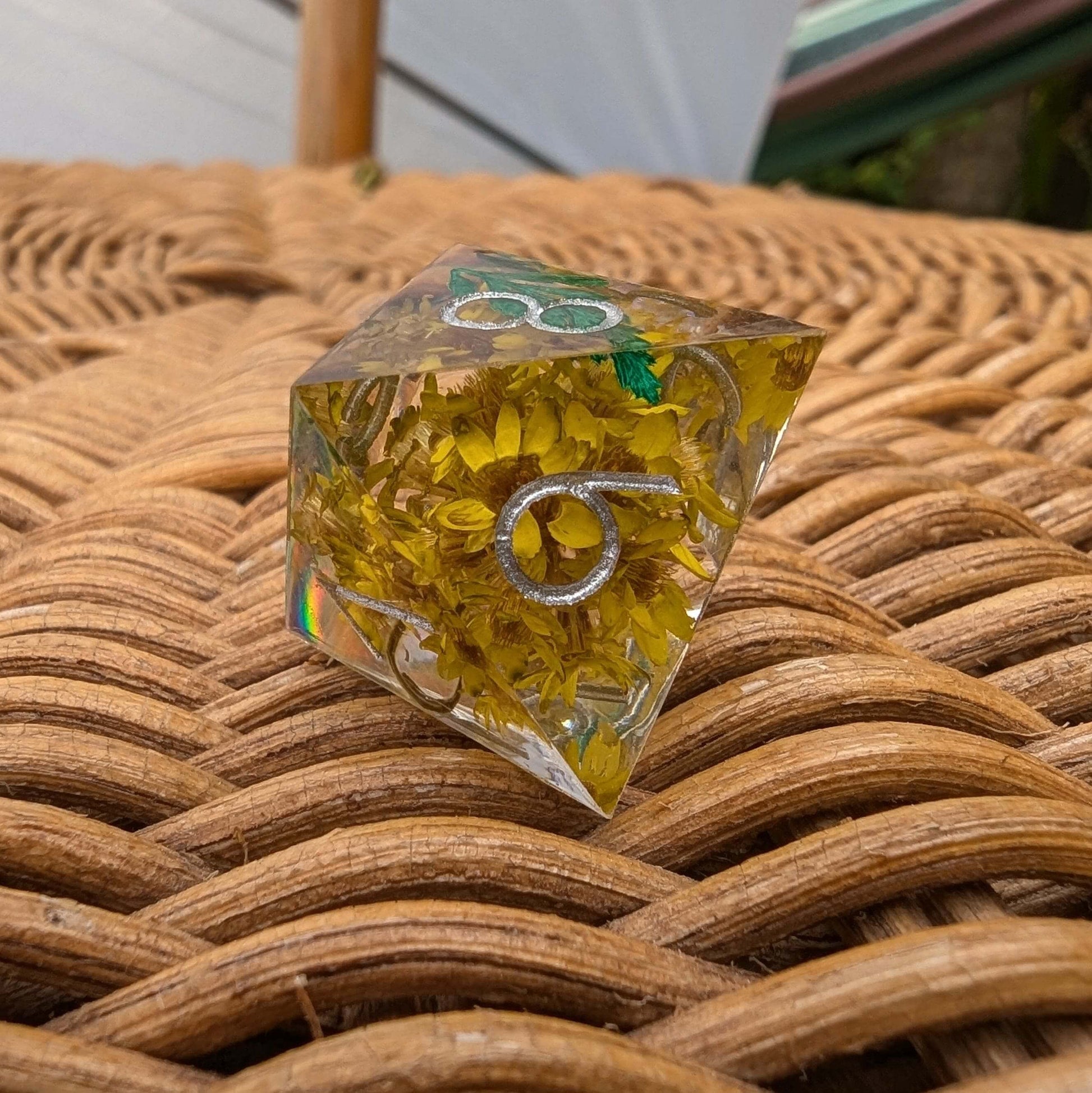 Enchanted Meadow sharp edge DnD die with yellow flowers encased in clear resin and modern silver font on a woven mat.