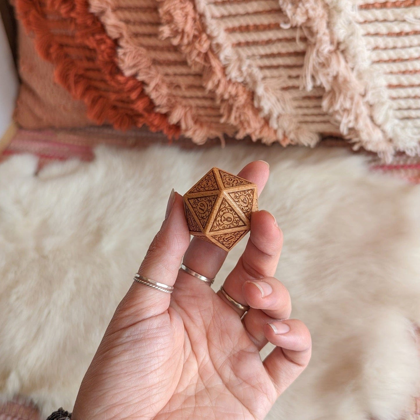 Hand holding a large wood D20 die with intricate filigree art, set against a cozy background. Ideal for Dungeons and Dragons fans.