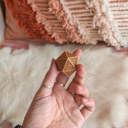 Hand holding intricately designed wood D20 dice with art nouveau details, ideal for Dungeons and Dragons gaming sessions.