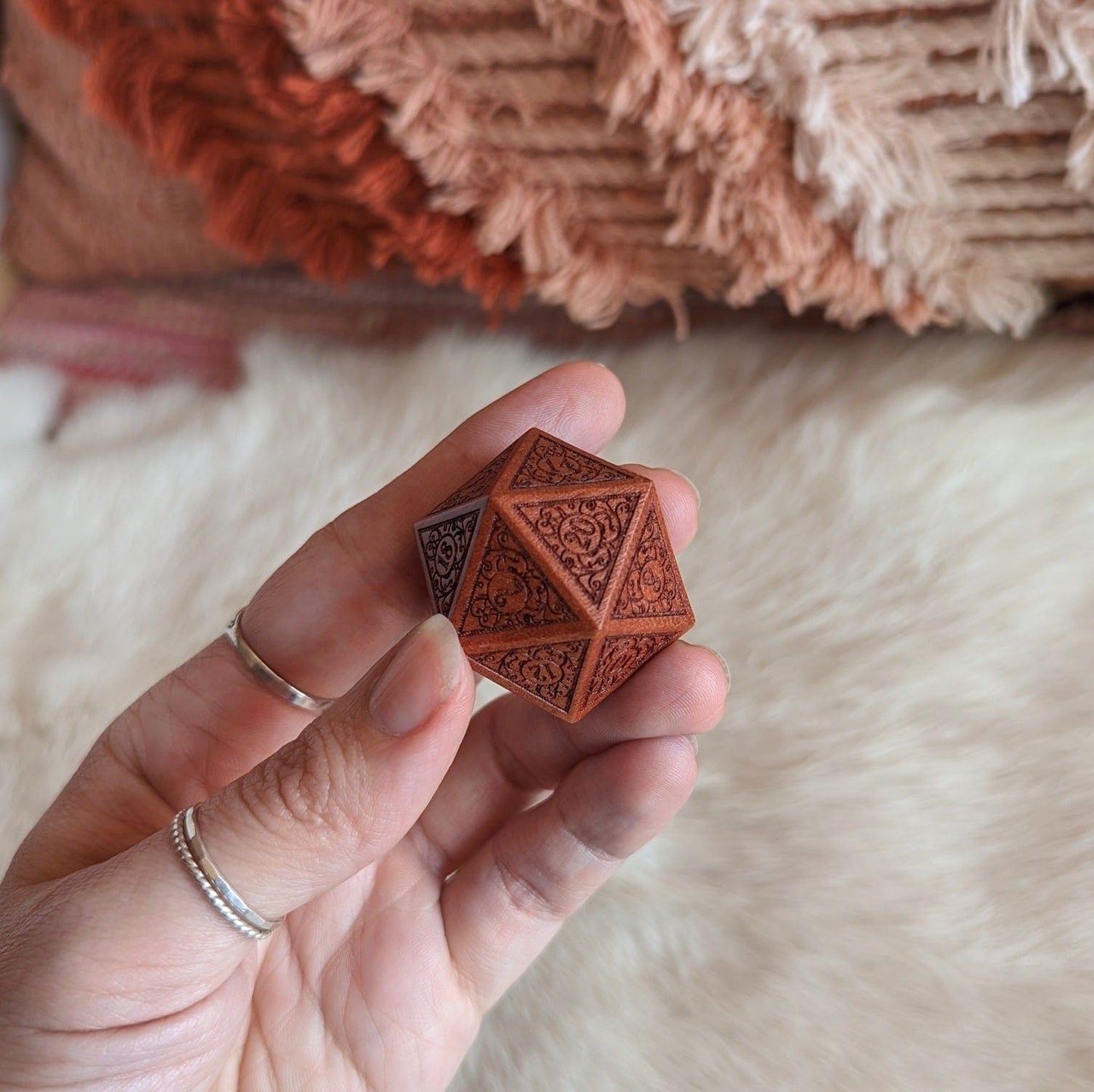 Hand holding intricately carved wooden D20 die with art nouveau design, perfect for enhancing tabletop role-playing games.