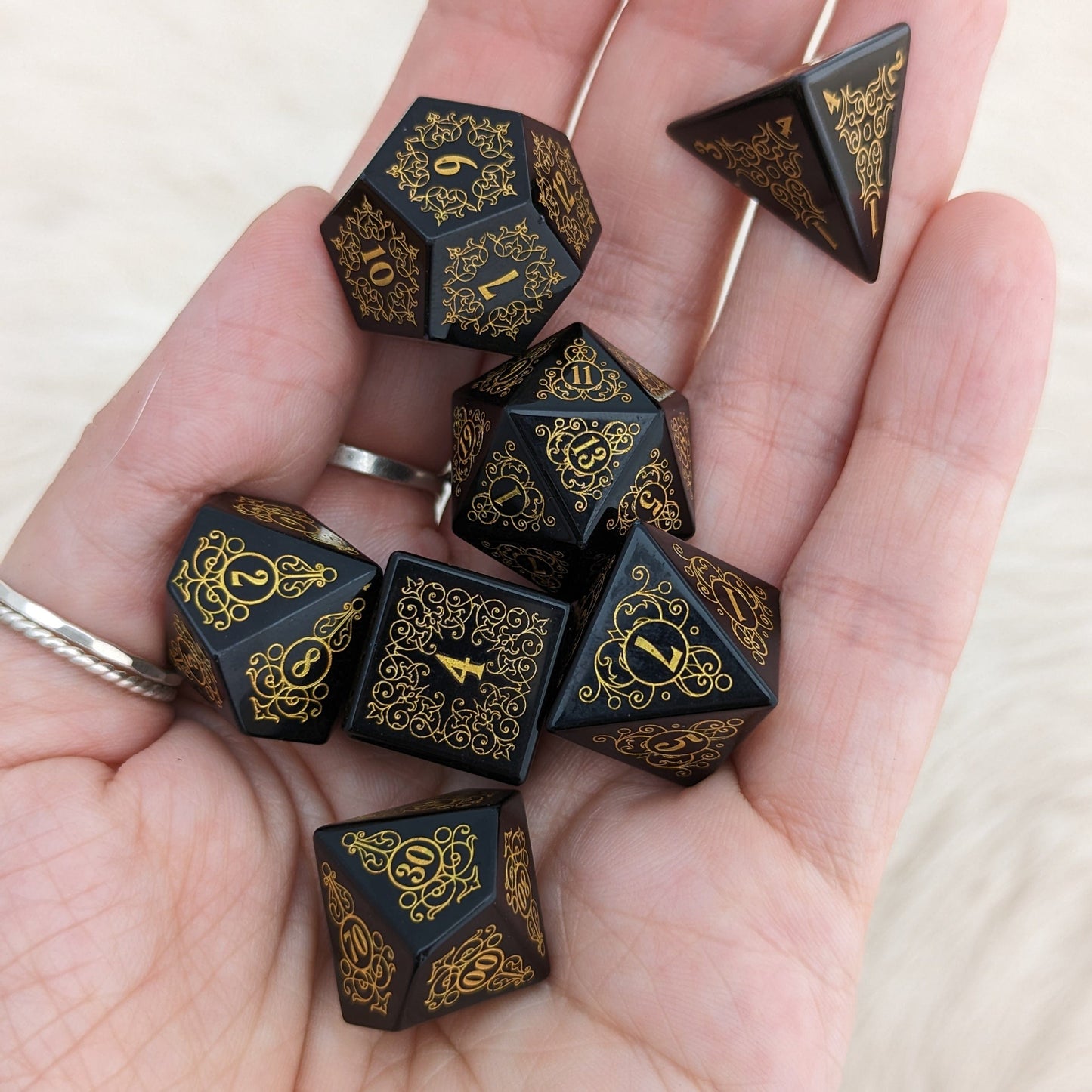 Hand holding Garden Gate Obsidian Gemstone Dice Set with intricate golden floral designs.