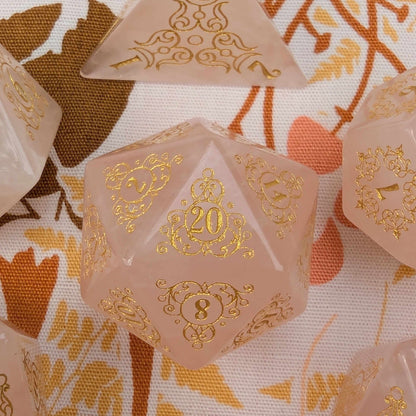 Rose quartz dice set with gold numbers on floral design background, showcasing intricate garden gate patterns and enchanting elegance.