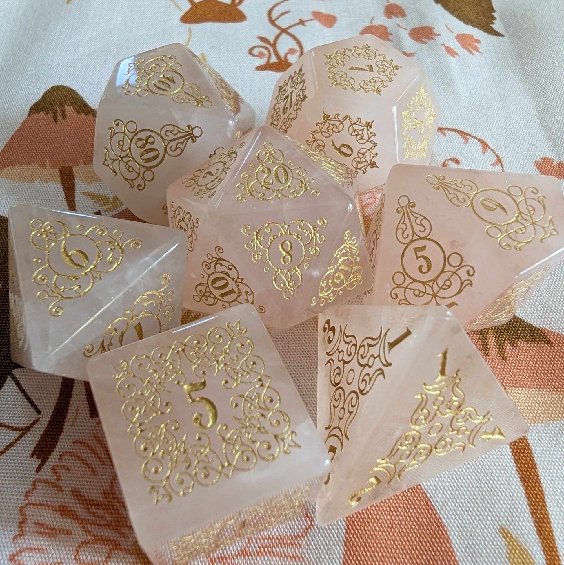 Rose quartz dice set with gold font, featuring intricate floral designs, inspired by nature's enchantment and elegance.