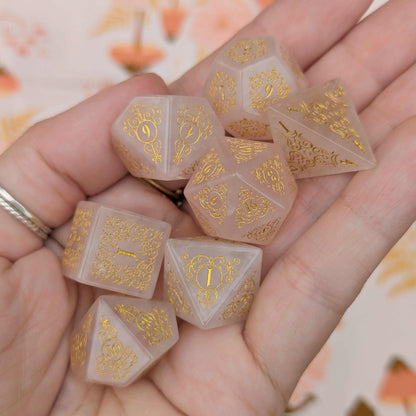 Rose Quartz Gemstone Dice Set with Gold Font held in hand, featuring intricate floral designs inspired by nature's enchanting beauty.