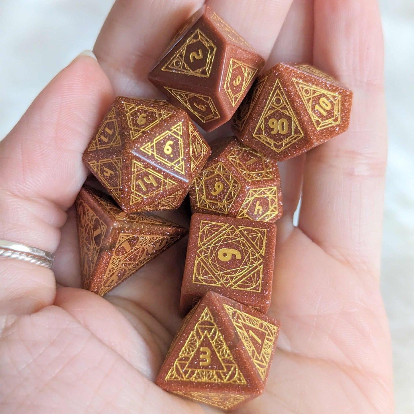 A hand holding a set of seven Geometric Goldstone dice with etched numbers, ideal for tabletop RPGs.