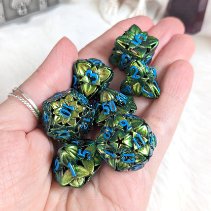 Hand holding green floral hollow metal dice set with blue numbers for tabletop RPGs.