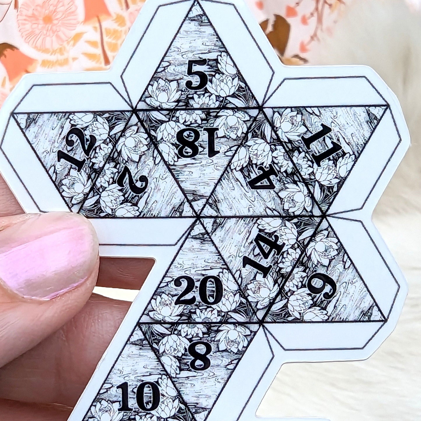 Black and white lily pad D20 sticker with numbers, held in hand, perfect for decorating laptops or journals.