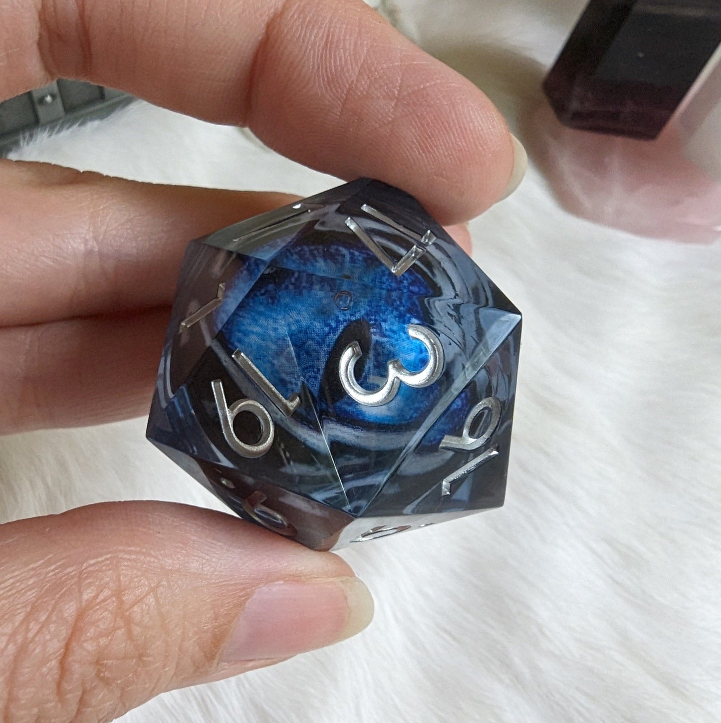 Blue and black liquid core eye D20 die held in hand, perfect for tabletop games like Dungeons and Dragons.