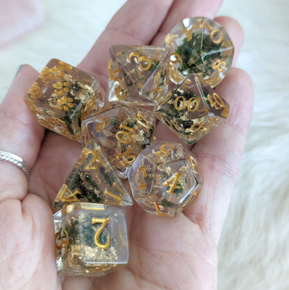 Hand holding Moss and Gold Dice Set with real dried plants, featuring gold font, 8 polyhedral dice for DND and TTRPGs.