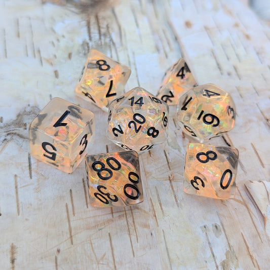 Phoenix's Rebirth TTRPG Dice Set with iridescent orange cellophane in clear resin, showcasing black numbers on wooden background.