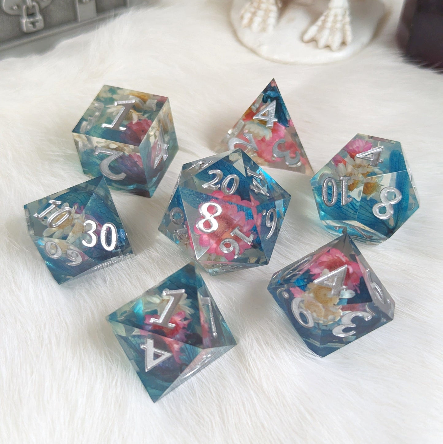 Pink, white, and blue floral DnD dice set with silver numbers, featuring seven TTRPG dice on a white background.