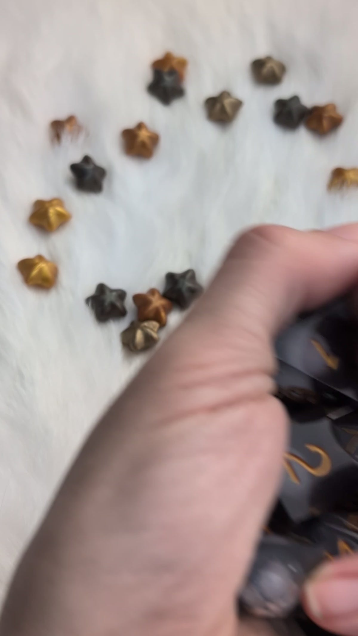 A set of translucent smoky gray polyhedral gaming dice with metallic gold numbers being shook in a hand to display the liquid moving on the inside