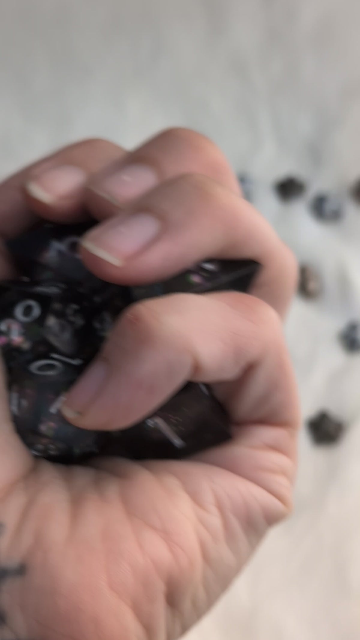 A set of translucent dark gray polyhedral gaming dice with holographic glitter and white numbering in a video held in a hand moving around the dice to show the different angles 