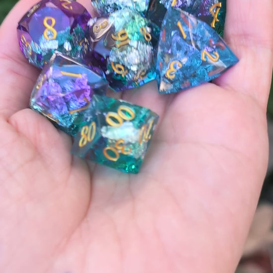A set of translucent polyhedral gaming dice with gold numbers, displayed in a person's hand in a video with the dice being moved around to show off the different angles
