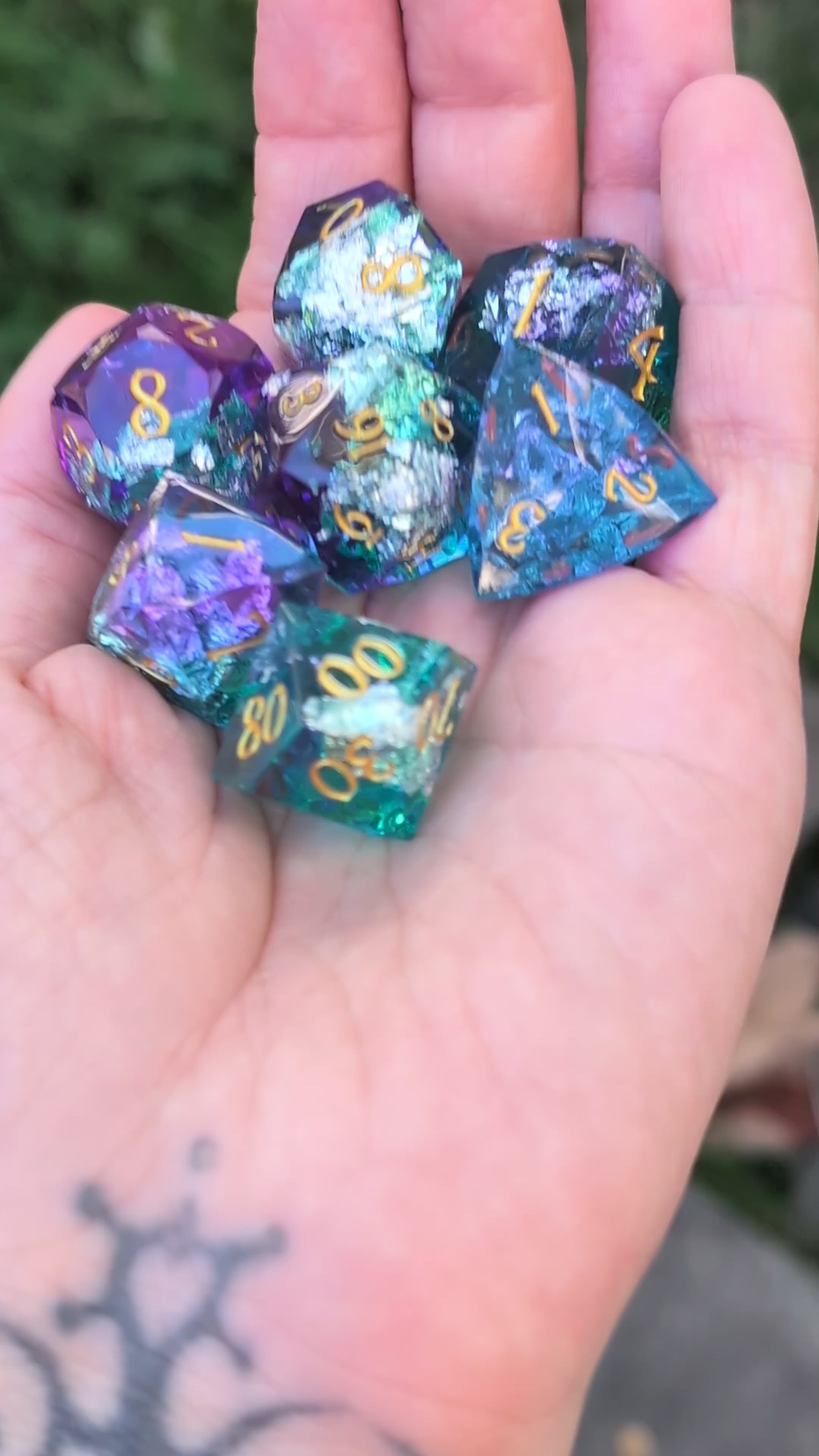 A set of translucent polyhedral gaming dice with gold numbers, displayed in a person's hand in a video with the dice being moved around to show off the different angles