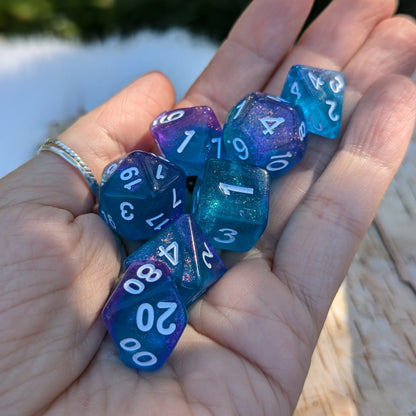 Hand holding Purple and Blue Will O Wisp 7-piece glitter polyhedral dice set for tabletop RPGs like Dungeons and Dragons.