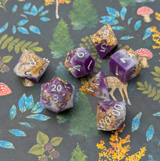 Royal Amethyst DnD Dice Set with purple, white, and gold foil details on a decorative forest-themed background.