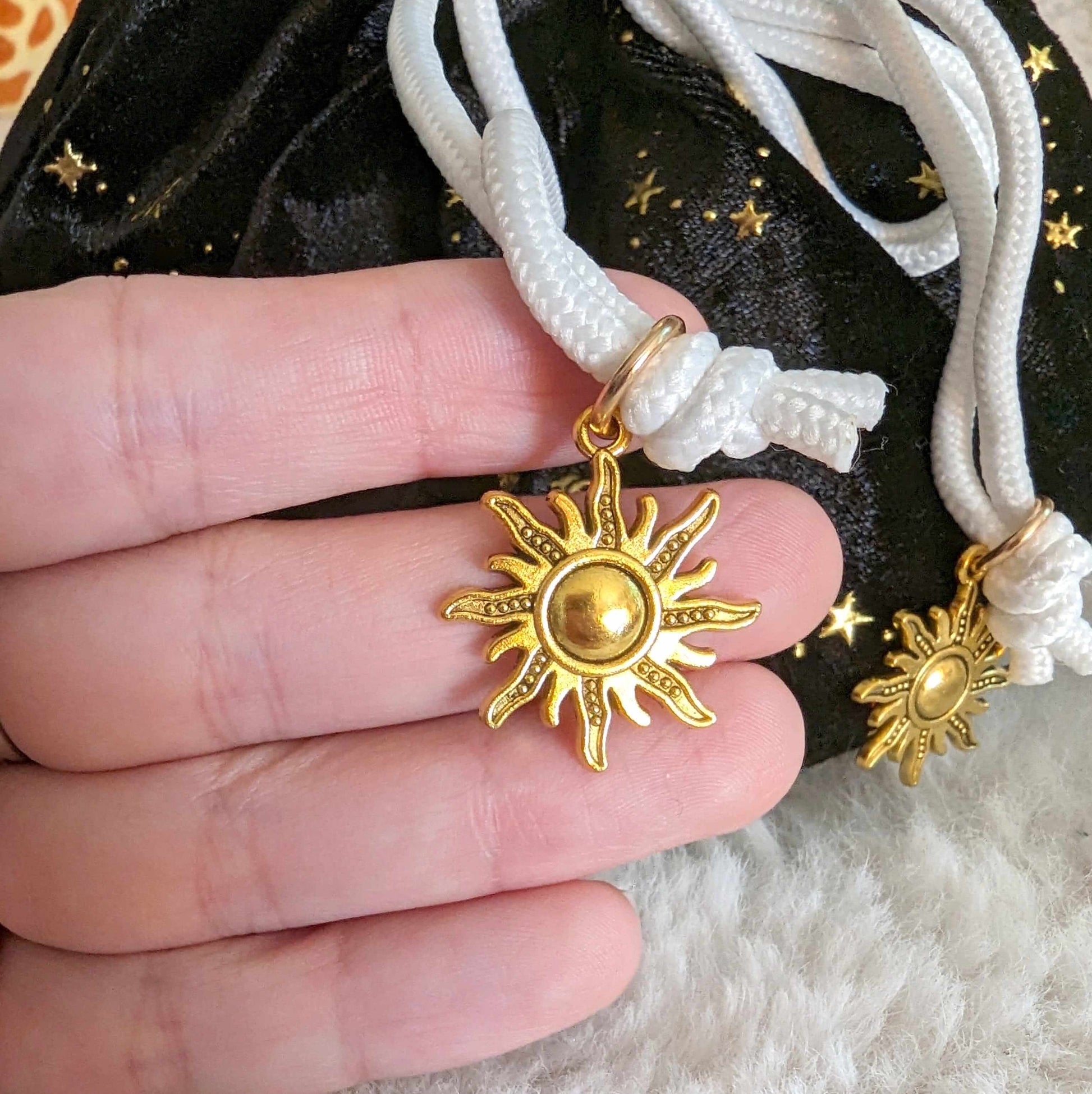 Gold sun charm on white cord of starry black dice bag with multi pockets and plush lining for tabletop gamers.