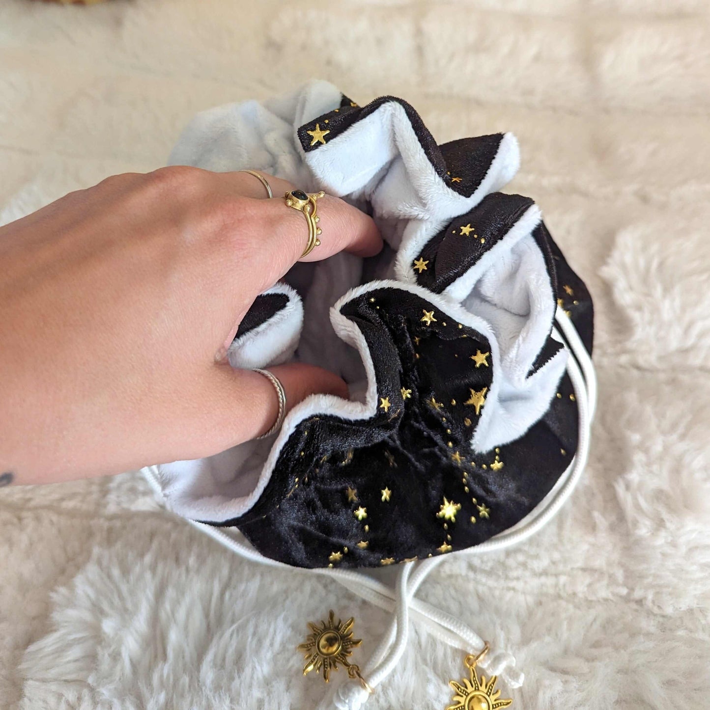 Luxurious black velvet dice bag with golden stars and sun charms, featuring soft white lining and multiple pockets.