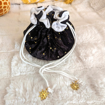 Starry black velvet dice bag with golden stars, white plush lining, and sun charm drawstrings on a soft background.