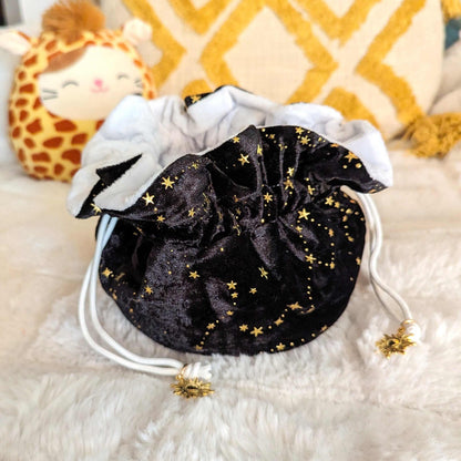 Black velvet dice bag with golden stars, white plush lining, and drawstring cords accented with golden sun charms, ideal for tabletop gamers.